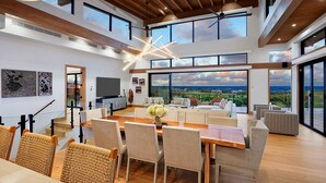 Ampla sala de estar com uma grande mesa de jantar de madeira, assentos confortáveis e vista para a paisagem por grandes janelas.