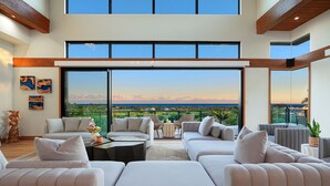 Ampla sala de estar com uma grande janela que oferece uma vista panorâmica, mobiliada com sofás e uma mesa de centro.