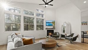 Un salon spacieux doté d ’une grande fenêtre, d’une cheminée, d’un téléviseur et d’un ventilateur de plafond.