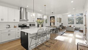 Une cuisine moderne avec des meubles blancs, des appareils en acier inoxydable et un îlot central doté de tabourets de bar.