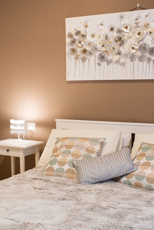 Un dormitorio con cama, mesita de noche con lámpara y un cuadro abstracto colgado en la pared.
