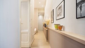 Un pasillo con una puerta blanca, una recepción con cuadros enmarcados y un mostrador con objetos decorativos.
