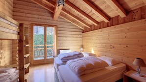 A wooden cabin bedroom with a bed, a nightstand, a lamp, and a window with a view of greenery.