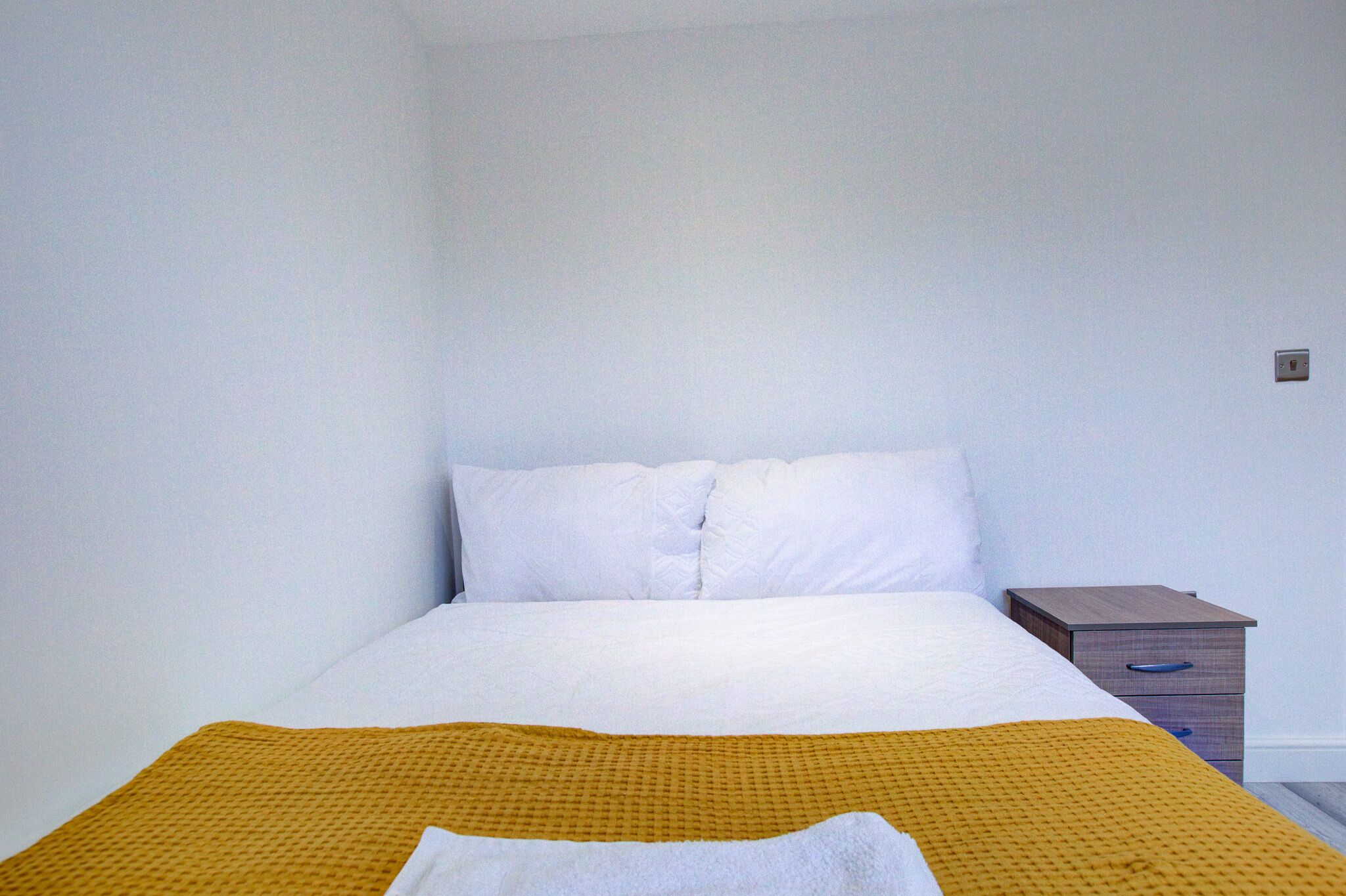 A single bed with white bedding and a mustard-colored throw blanket.