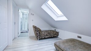 Una camera da letto con soffitto spiovente, una finestra a lucernario, un divano a motivi zebrati e un letto decorato.
