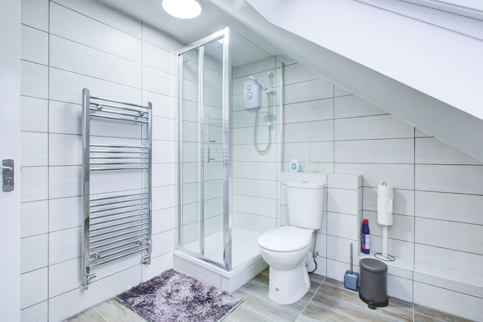 A modern bathroom with a glass-enclosed shower, a white toilet, and a towel rack.