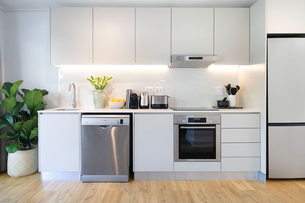 A modern kitchen with white cabinetry, stainless steel appliances, and a built-in oven.