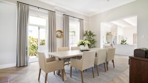 A dining area with a wooden table, six chairs, a rug, and a potted plant. - Middedorp Villa and Apartments (Stellenbosch)