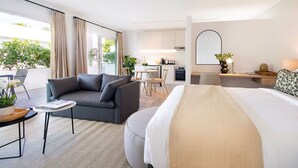 A modern hotel room with a sofa, a bed, a dining area, and a kitchen in the background. - Middedorp Villa and Apartments (Stellenbosch)