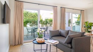 A modern living room with a grey sofa, a small round table with a magazine, and a potted plant. - Middedorp Villa and Apartments (Stellenbosch)