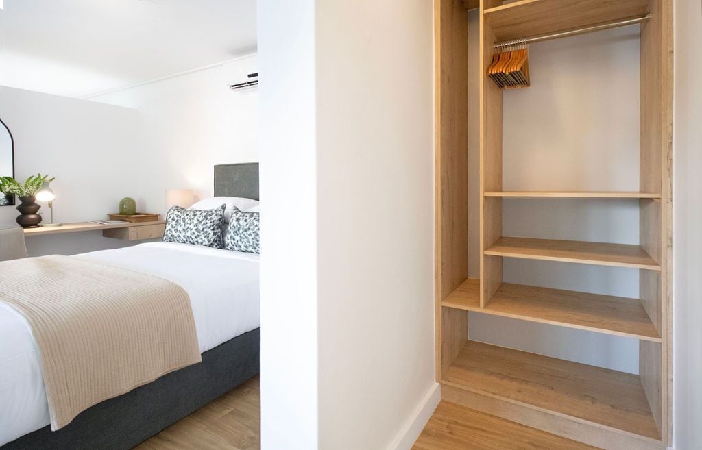 Une chambre à coucher avec un lit, une table de chevet, une lampe et une petite plante. La pièce a un mur blanc et un plancher en bois.