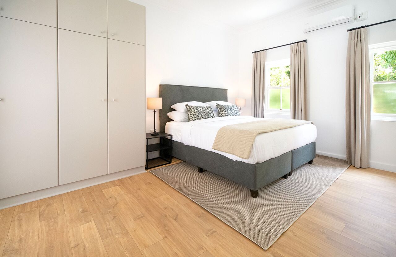 Un dormitorio con cama, mesitas de noche, armario y ventana con cortinas.