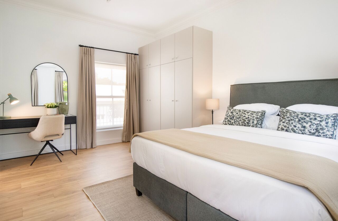 A bedroom with a bed, a desk, a chair, a wardrobe, and a window with curtains.