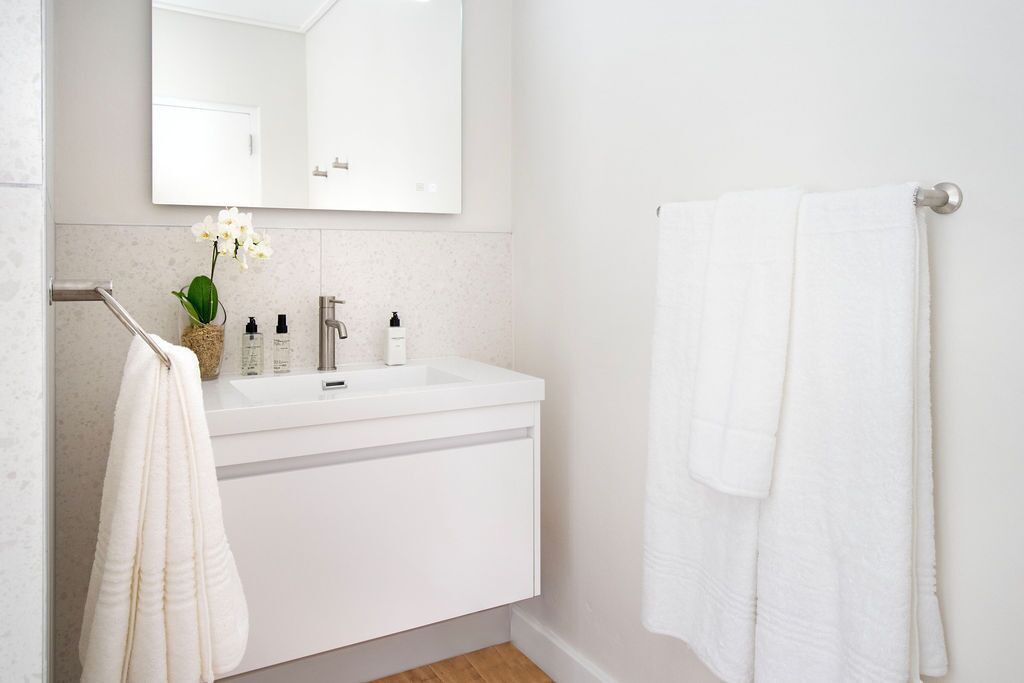 Un baño moderno con lavamanos, espejo y toallero blancos.