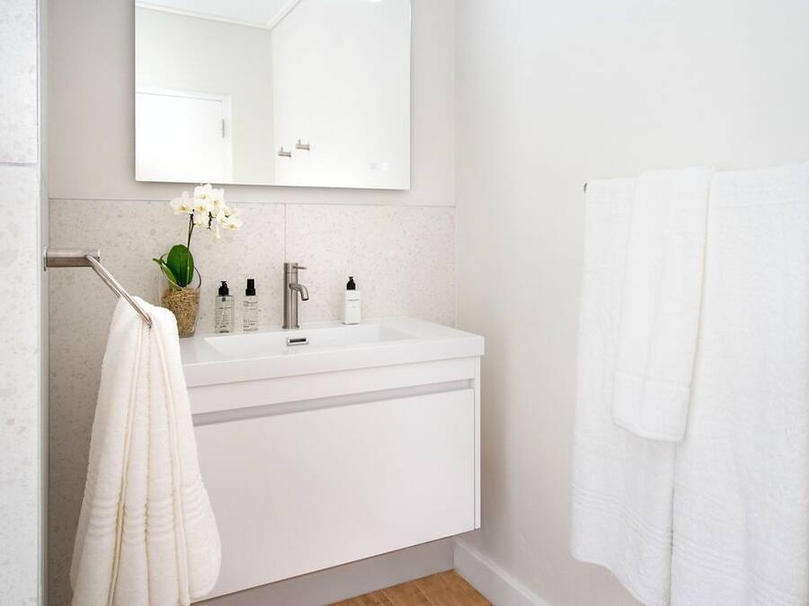 Un baño moderno con lavamanos, espejo y toallero blancos.
