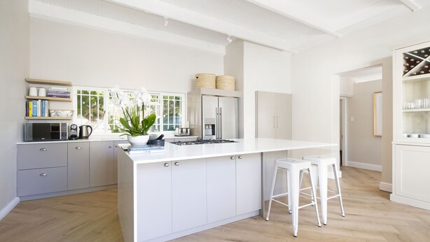 A modern kitchen with white cabinetry, a large island, and bar stools. - Middedorp Villa and Apartments (Stellenbosch)