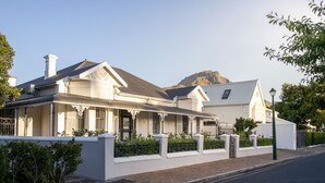 A white colonial-style house with a prominent chimney, a balcony, and a mountain in the background. - Middedorp Villa and Apartments (Stellenbosch)