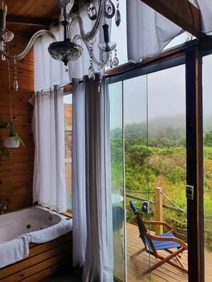 A wooden cabin with a glass-enclosed balcony, a wooden deck, and a bathtub.