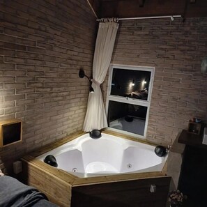 A room with a brick wall, a window with a curtain, and a wooden bathtub. - O Chale Encantado (Rancho Queimado)