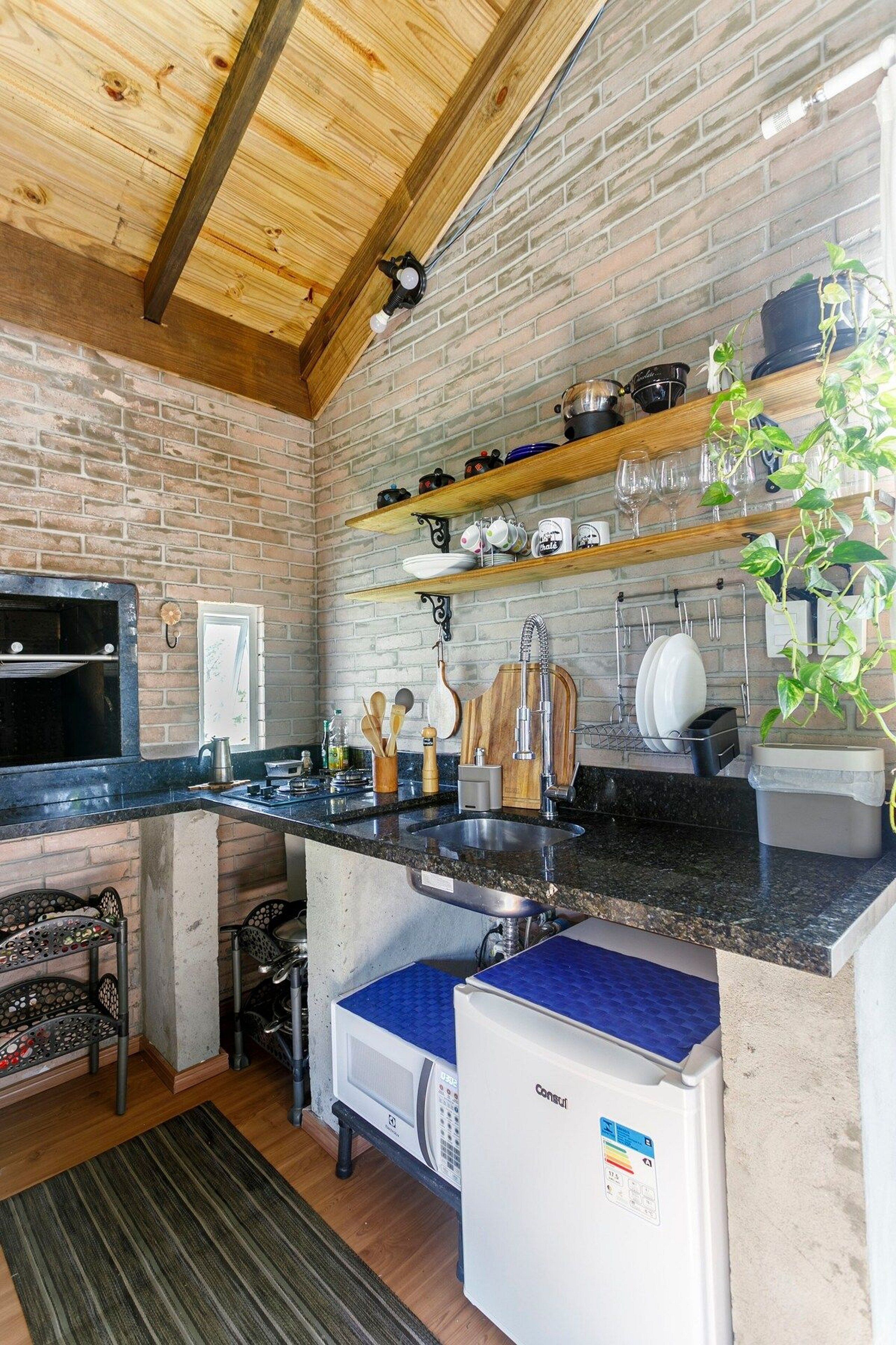 A compact kitchen with a brick wall, wooden beams, a built-in oven, and a compact refrigerator.