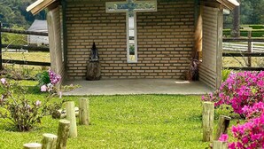 A small brick chapel with a cross, surrounded by a grassy area and wooden posts. - O Chale Encantado (Rancho Queimado)
