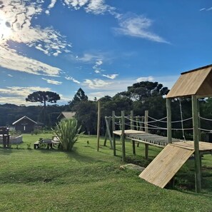 A playground with wooden structures and rope bridges, surrounded by grass and trees. - O Chale Encantado (Rancho Queimado)