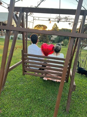 A wooden swing set in a grassy area with a house in the background. - O Chale Encantado (Rancho Queimado)