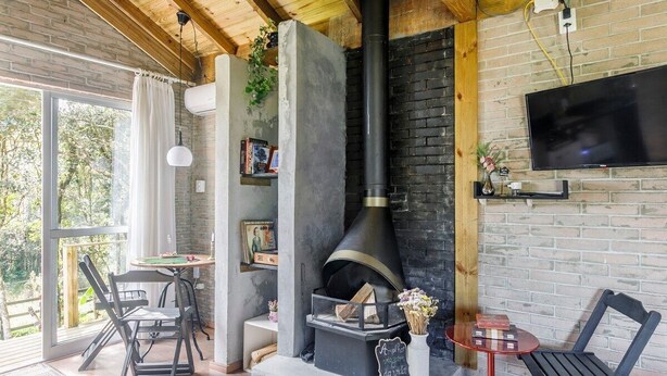 A cozy room with a fireplace, a television, and a dining area with chairs and a table. - O Chale Encantado (Rancho Queimado)