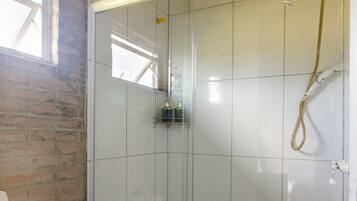 A bathroom with a glass shower enclosure, a white toilet, and a wooden ceiling.