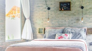A cozy bedroom with a brick wall, a wooden ceiling, and a bed with a pink blanket. There are two wall-mounted lights and a window with curtains. - O Chale Encantado (Rancho Queimado)