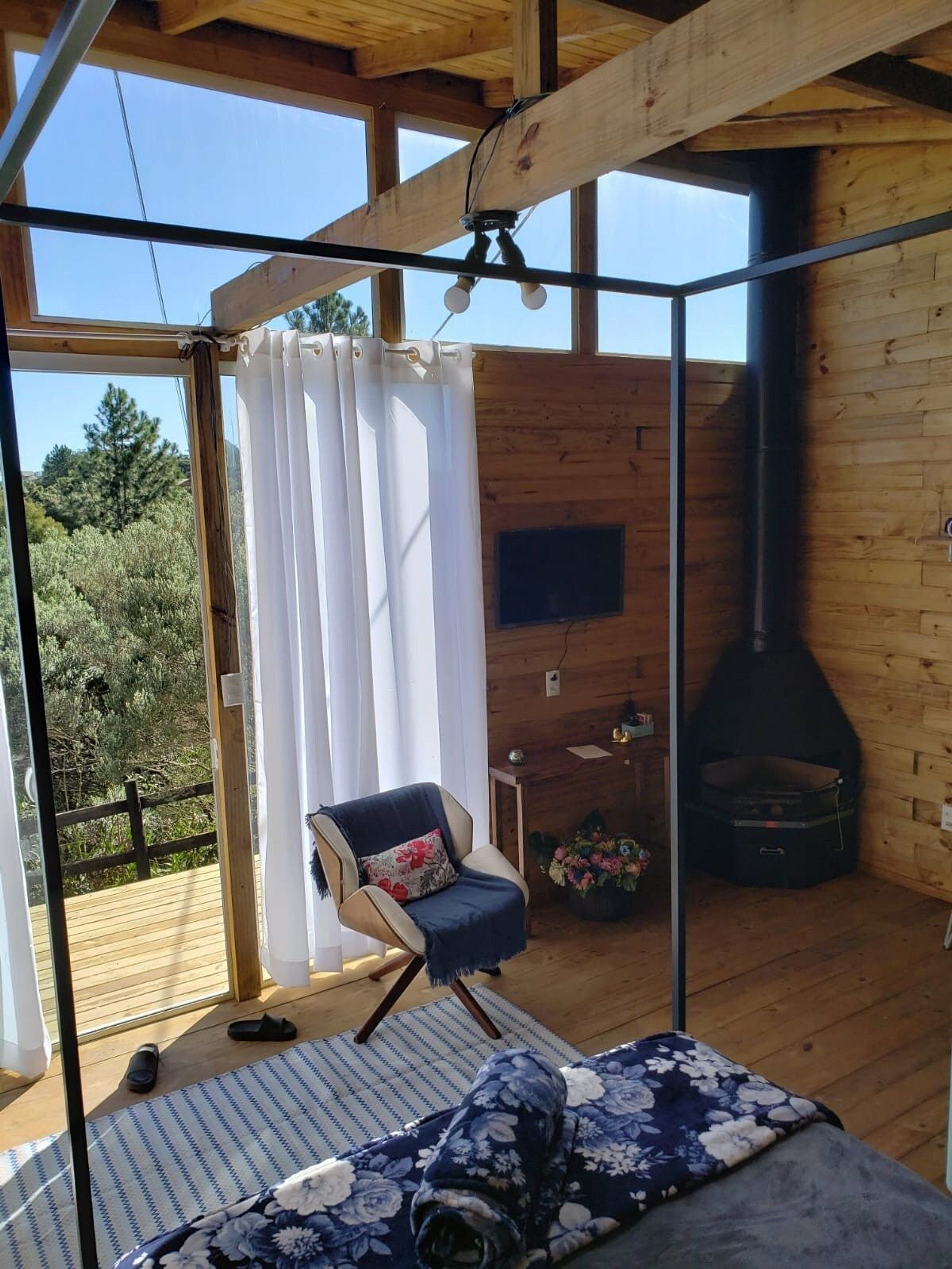 Une pièce chaleureuse avec un plafond en bois, un fauteuil avec un coussin, un canapé, une cheminée et une vue sur l’extérieur.