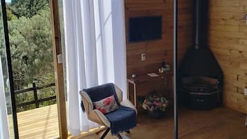 Une pièce chaleureuse avec un plafond en bois, un fauteuil avec un coussin, un canapé, une cheminée et une vue sur l’extérieur.