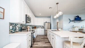 Une cuisine moderne avec des meubles blancs, un grand îlot central et un pare-feu orné de carreaux bleus.