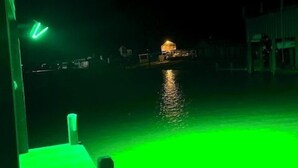 Vue nocturne d’une propriété située au bord de l’eau, avec une terrasse en bois et une piscine.