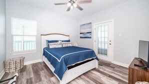 Une chambre à coucher avec un lit, un ventilateur de plafond, une télévision et une fenêtre avec des stores.