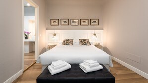 A bedroom with a large bed, two bedside tables with lamps, a black bench with towels, and framed pictures on the wall. - San Pier Maggiore Abbess's Suite (Firenze)