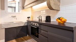A modern kitchen with dark cabinetry, a wooden floor, a built-in oven, and a kettle on the counter. - San Pier Maggiore Abbess's Suite (Firenze)