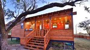 Une cabane en bois avec un escalier menant à une terrasse, entourée d’un sentier pavé de pierres et d’un arbre.