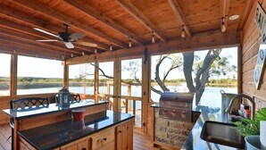 Une cabane en bois dotée d’un coin cuisine comprenant un barbecue, une table à manger et offrant une vue sur un lac.