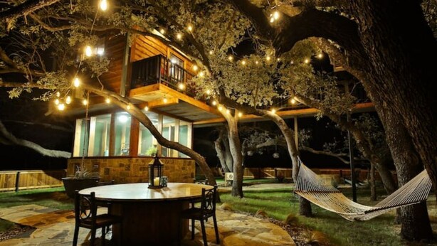 Ein Baumhaus mit einer runden Stein-Terrasse, einer Hängematte und Lichterketten.