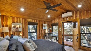 Ein Schlafzimmer einer Holzhütte mit Bett, Deckenventilator und großen Fenstern.