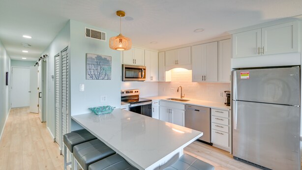 A modern kitchen with white cabinets, a stainless steel refrigerator, a microwave, and a large island with bar stools. - Murrells Inlet Condo w/ Balcony & Pool: Near Pier! (Murrells Inlet)