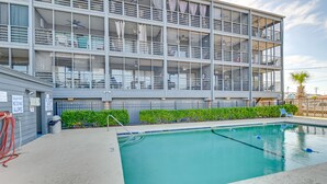 A multi-story hotel with a swimming pool, balconies, and a fenced area with greenery. - Murrells Inlet Condo w/ Balcony & Pool: Near Pier! (Murrells Inlet)