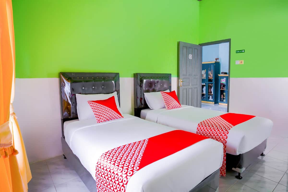 A hotel room with two beds, each with a headboard, white bedding, and red accents.