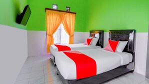 Una camera d'albergo con due letti, pareti verdi e una finestra con tende arancioni.