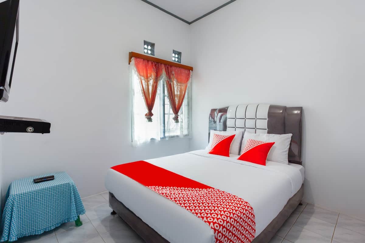 A modern bedroom with a large bed, red and white bedding, a small table with a checkered tablecloth, and a window with red curtains.