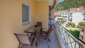Ein Balkon mit Tisch und Stühlen, ein Fenster und Blick auf Gebäude sowie einen Hügel.