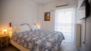 Ein Schlafzimmer mit Bett, Nachttisch, Lampe, Klimaanlage, Fenster mit Spitzenvorhängen und einem Bild an der Wand.