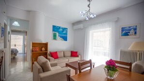 Ein modernes Wohnzimmer mit einer Couch, einem Esstisch und Stühlen. Es gibt ein Bücherregal und ein Fenster mit Vorhängen.