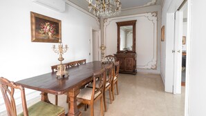 Une salle à manger avec une table en bois, des chaises, un lustre, un miroir et un tableau accroché au mur.